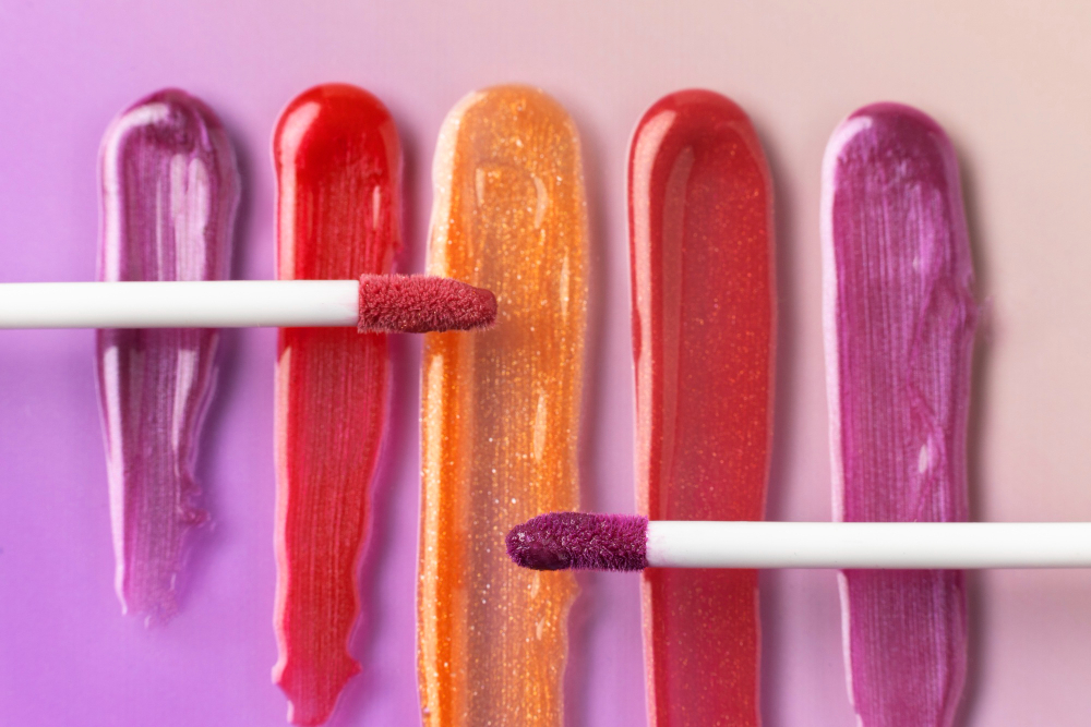 Muestras de brillos labiales en tonos vibrantes con aplicadores sobre fondo rosa