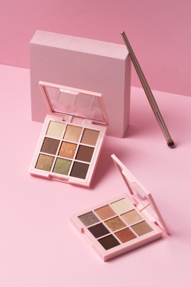 Paleta de sombras con tonos nude y espejo abierto sobre fondo rosa